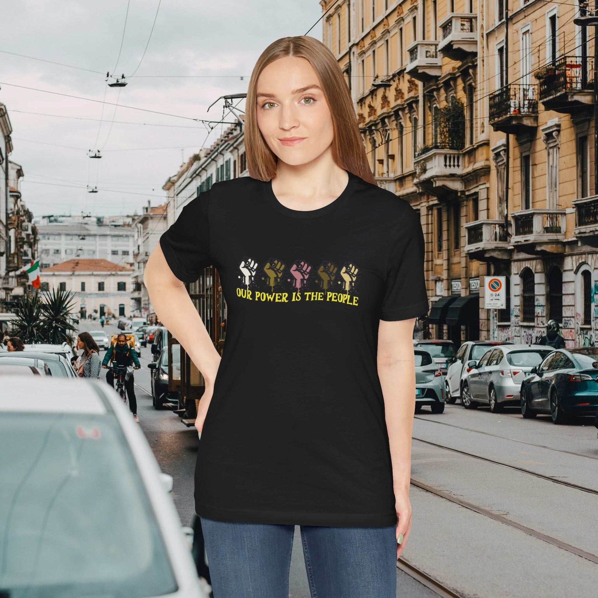 Empowering text 'Our Power is the People' with diversity raised fist worn by a woman, on a black tee, city background