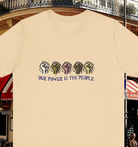 Empowering text 'Our Power is the People' with diversity raised fist on a soft cream color tee, city background