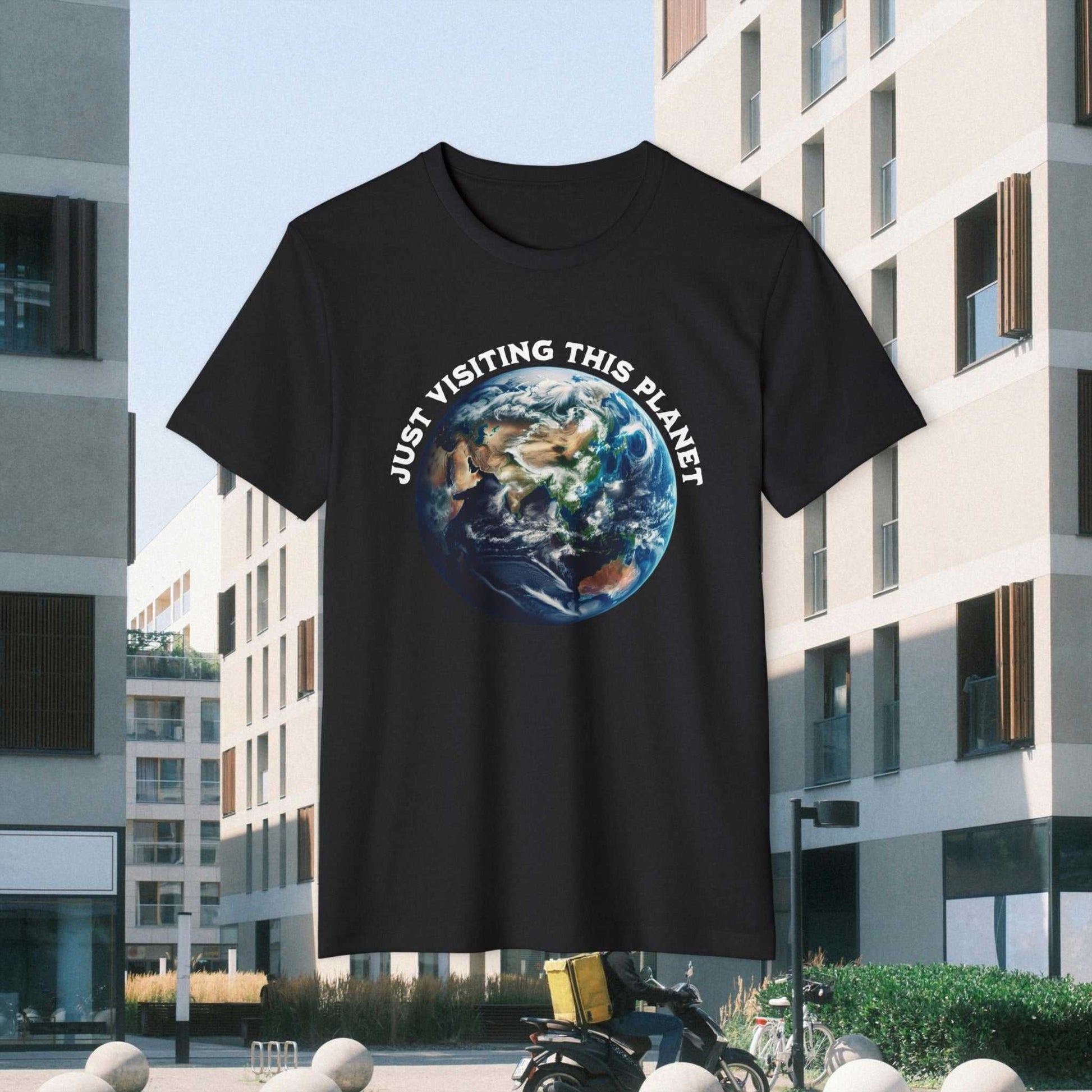 Just Visiting This Planet text w Earth graphic on a black Tee