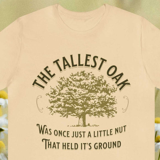 Stubborn. The tallest oak was once just a little nut that held it's ground - text surrounding an oak tree graphic, on a tan t-shirt.