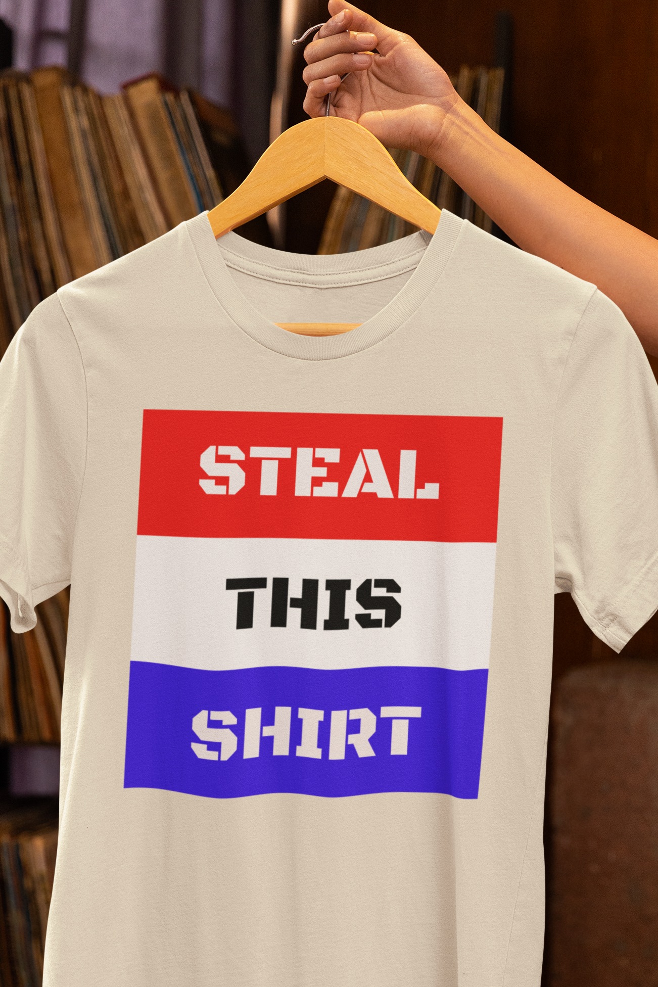 STEAL THIS SHIRT text with red white and blue background on a heather natural colored tee